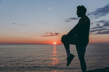Silhouette side view young strong sporty athletic toned fit sportsman man 20s wear sports clothes warm up training at sunrise sun dawn over sea beach outdoor on pier seaside in summer day morning.