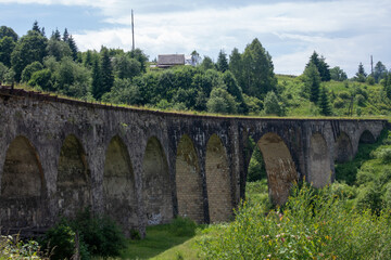 Fototapeta premium Old viaduct in Vorokhta, Carpathians. View from the bridge to the bend and the columns below surrounded by lush greenery
