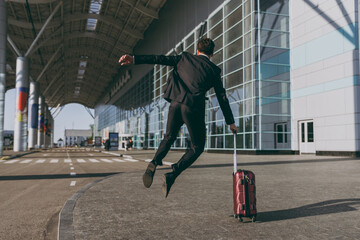 Back rear view full length young traveler businessman man in black dinner suit stand outside at international airport terminal with suitcase valise jumping high Air flight business trip concept