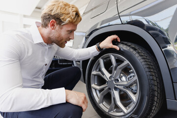 Fototapeta na wymiar Side view man customer male buyer client in white shirt chooses auto wants to buy new automobile touch car tire wheel disk in showroom vehicle salon dealership store motor show indoor Sales concept.
