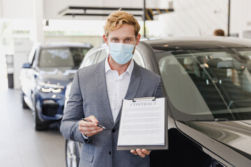 Fototapeta na wymiar Man serious customer male client buyer in classic grey suit pandemic mask choose auto want buy new car automobile sign paper document in showroom salon dealership store motor show indoor Sale concept