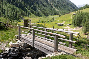 Fototapeta na wymiar Wooden bridge over a small stream in the Alps. Mountain landscape