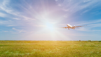 Passenger plane over a green field in a beautiful blue sky. The sun shines brightly. Summer landscape. Transport, travel