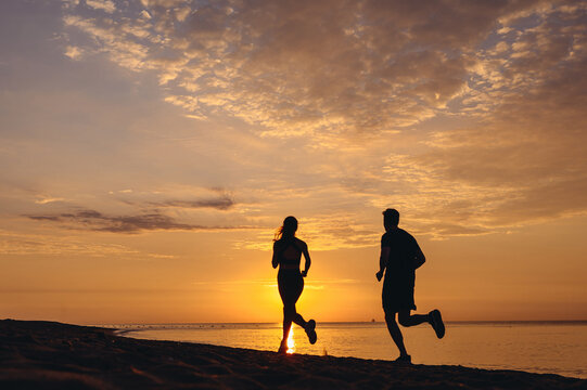 Full size back view couple young friends sporty sportsman sportswoman woman man in sport clothes warm up training running jog on seaside sunrise over sea sand ocean beach outside in summer day morning