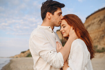Fototapeta premium Side view close up smiling happy young lovely couple two friends family man woman in casual clothes hug each other kiss forehead at sunrise over sea beach outdoor seaside in summer day sunset evening