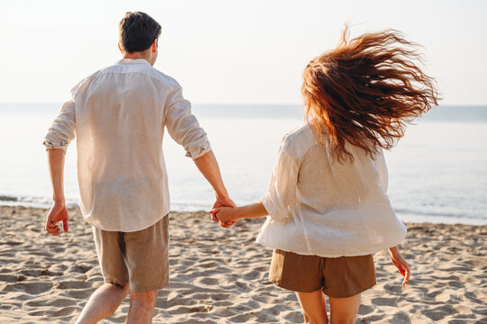 Back view young couple two friends family man woman in white shirt clothes running to water hold hands rest relax together at sunrise over sea beach ocean outdoor exotic seaside in summer day evening
