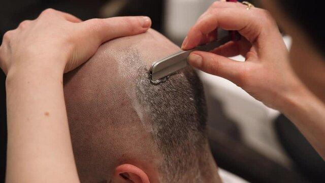 barber shaves a man's head with a straight razor