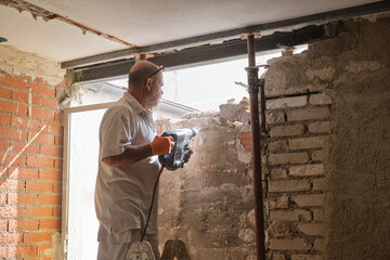 Builder with demolition hammer breaking a house wall.