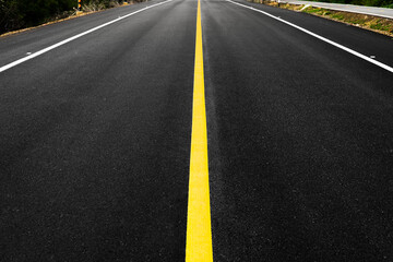 Close up of local black asphalt road surface texture with a separation yellow line. Selective focus.