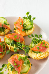Delicious hearty appetizer, salmon toast on a white plate, round fried bun with red fish, cucumber, hollandaise sauce and pea sprouts