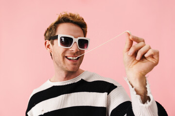 Ginger young man wearing sunglasses stretching bubblegum