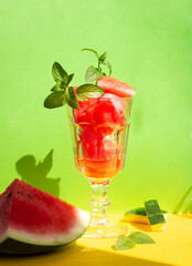 summer refreshing dessert, pieces of watermelon mixed with ice in a vintage glass on bright green and yellow background