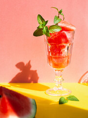 summer refreshing dessert of pieces of watermelon mixed with ice in a vintage goblet on bright pink and yellow background, harsh sun light and shadows