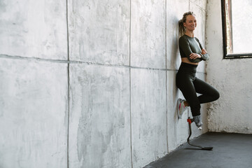 Fototapeta premium Young sportswoman with prosthesis smiling while leaning on wall