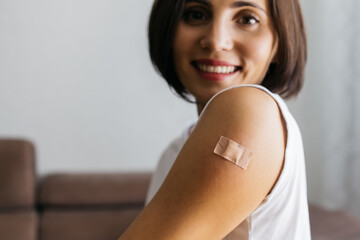 Portrait of smiling woman after getting a vaccine. Female holding down her white shirt sleeve and...