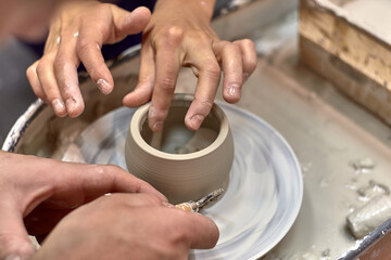 Fototapeta na wymiar The hands of a man who learns to trim the edges of a product on a potter's wheel and his ceramist teacher