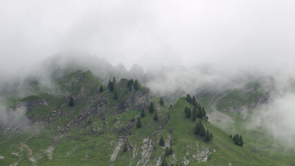 Summer scene in the Swiss Alps on a rainy, misty day. Steep green meadows and mountain ridge.