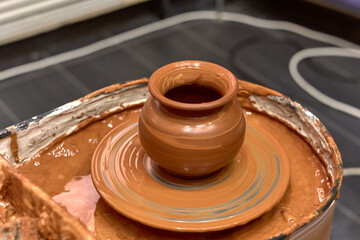 Freshly made red clay pot stands on a wet potter's wheel