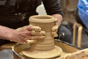 Fototapeta na wymiar Hands of a ceramist in the process of making a large vase of light clay on a potter's wheel