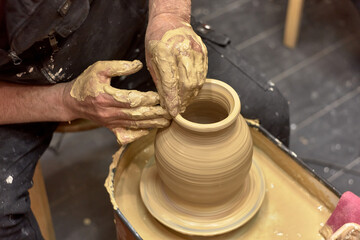Hands of a ceramist in the process of making a large vase of light clay on a potter's wheel