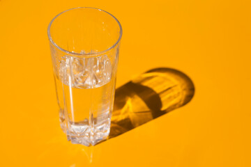 A glass of water on a yellow background. In the sunlight and with a shadow.