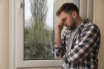 Depressed man near window at home. Space for text