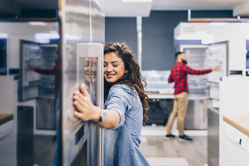 Young woman choosing new fridge for her home in store.