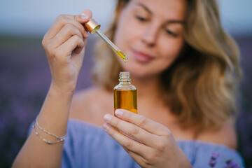 Woman holding bottle with natural essential oil in a lavender field.