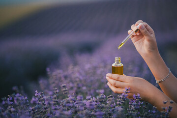 Woman holding bottle with natural essential oil in a lavender field.