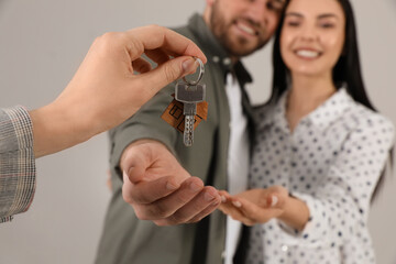 Real estate agent giving key to happy young couple against grey background, closeup