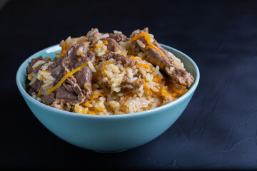 Uzbek national rice dish plov prepared on plate, dark background