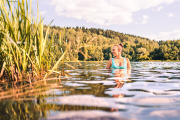 Lake in Finland. Happy smiling woman swimming in water summer. Finnish nature at sunset. Pretty girl in swimsuit or bikini enjoying a peaceful weekend or vacation outside at the beach in Scandinavia.