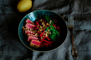 Tuna steak with linguine pasta, beetroot, hazelnut and ricotta sauce in blue bowl.