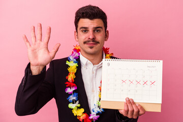 Young caucasian business man counting the days for vacations isolated on pink background smiling...