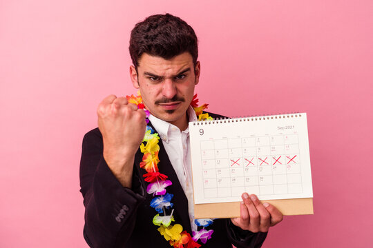 Young caucasian business man counting the days for vacations isolated on pink background showing fist to camera, aggressive facial expression.