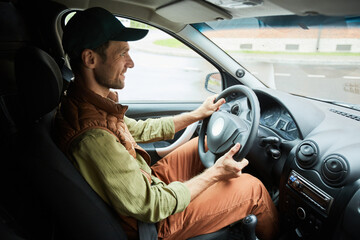 Side view portrait of smiling delivery worker driving van on road, copy space