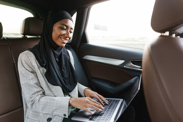 Black muslim woman working with laptop while going in car