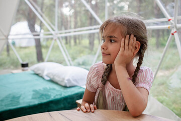 Cute girl looking through transparent bell tent with comfortable bed in forest, glamping hotel,...