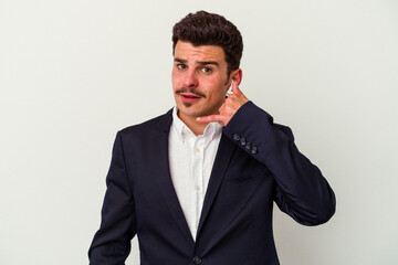 Young business caucasian man wearing wireless headphones isolated on white background showing a mobile phone call gesture with fingers.