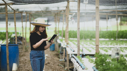 A teenage girl farmer uses a tablet app to control vegetable growing in greenhouse, smart farm.