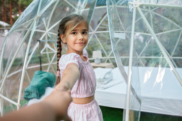 Cute girl looking through transparent bell tent with comfortable bed in forest, glamping hotel, luxury travel, glamourous camping with amenities, dome tent, feel at home in great outdoors lifestyle - obrazy, fototapety, plakaty