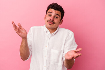 Young caucasian man isolated on pink background doubting and shrugging shoulders in questioning...