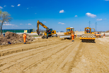 Road roller with spikes and earthmovers are working at construction site