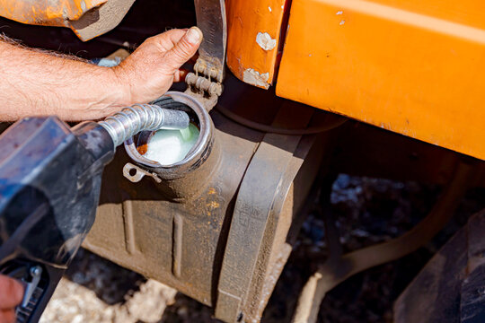 Hand holding handle fuel nozzle to refuel, petrol is pouring into the tank of an industrial mechanization