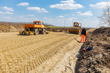 Road roller with spikes and truck plate compactor are working at construction site - obrazy, fototapety, plakaty