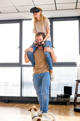 Positive man and woman play the game console with VR glasses at home, man holding wife on shoulders. Cheerful people having fun with new trends technology. Gaming concept. Video game. Copy space