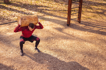 Muscular man doing squats with tree log outdoors - Powered by Adobe