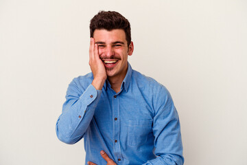 Young caucasian man isolated on white background laughs happily and has fun keeping hands on stomach.