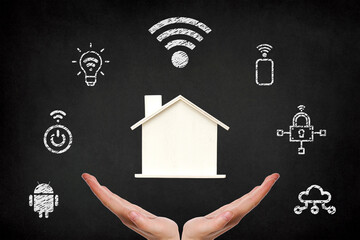 Smart home systems, hands holding a wooden house with smart home icons on blackboard