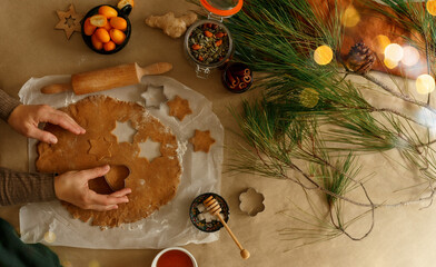 Home making Christmas gingerbread in the different form on a brown background. Hands holding cutting star shapes in cookie dough. 